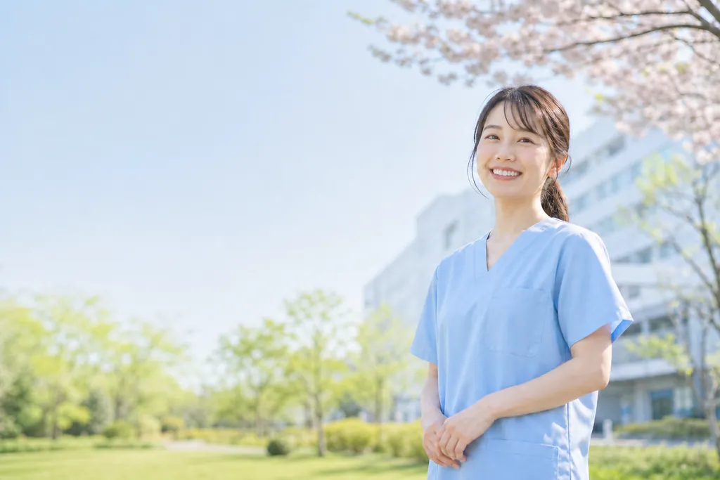 春の朝、桜と若葉の病院の庭で笑顔を見せる看護師